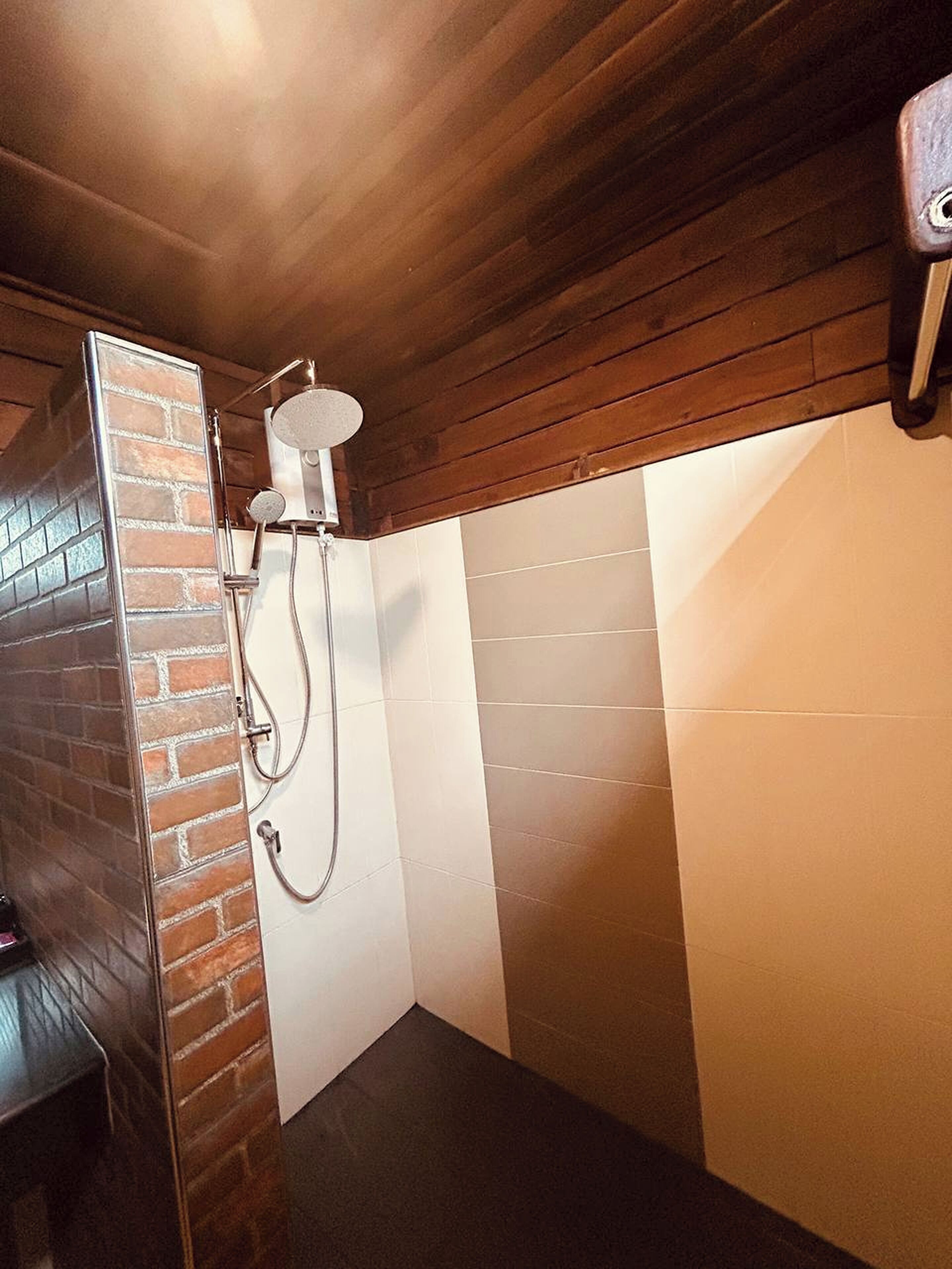 Baño con ducha, pared de ladrillo y techo de madera.