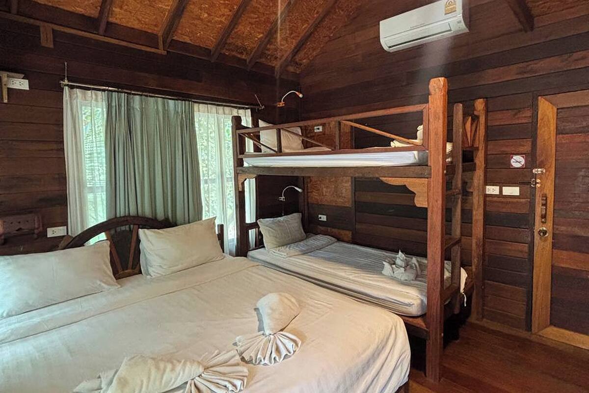 Ein Holzhütten-Zimmer mit einem Etagenbett, einem Einzelbett, einer Deckenleuchte und einer Klimaanlage.