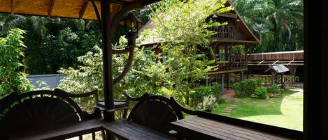 A wooden deck with benches overlooking a lush garden and a traditional wooden house.