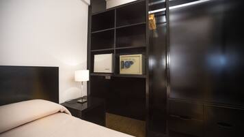 Ein Hotelzimmer mit Bett, Nachttisch, Lampe, Safe und Kleiderschrank.