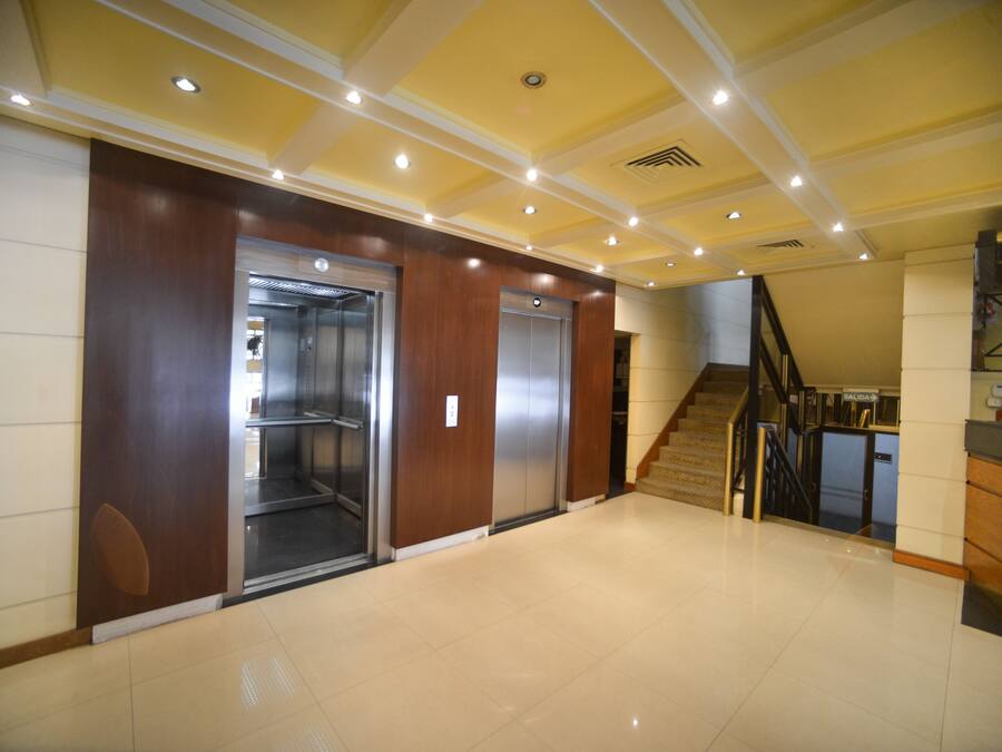 A spacious lobby with a modern elevator, a staircase, and a clean, tiled floor.