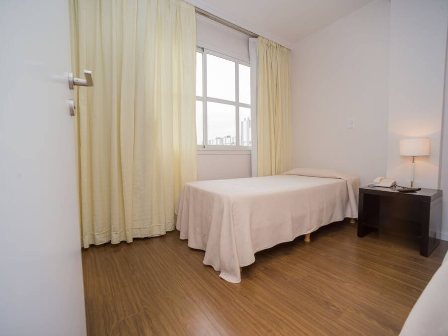 A room with a single bed, a nightstand with a lamp, and a window with curtains.