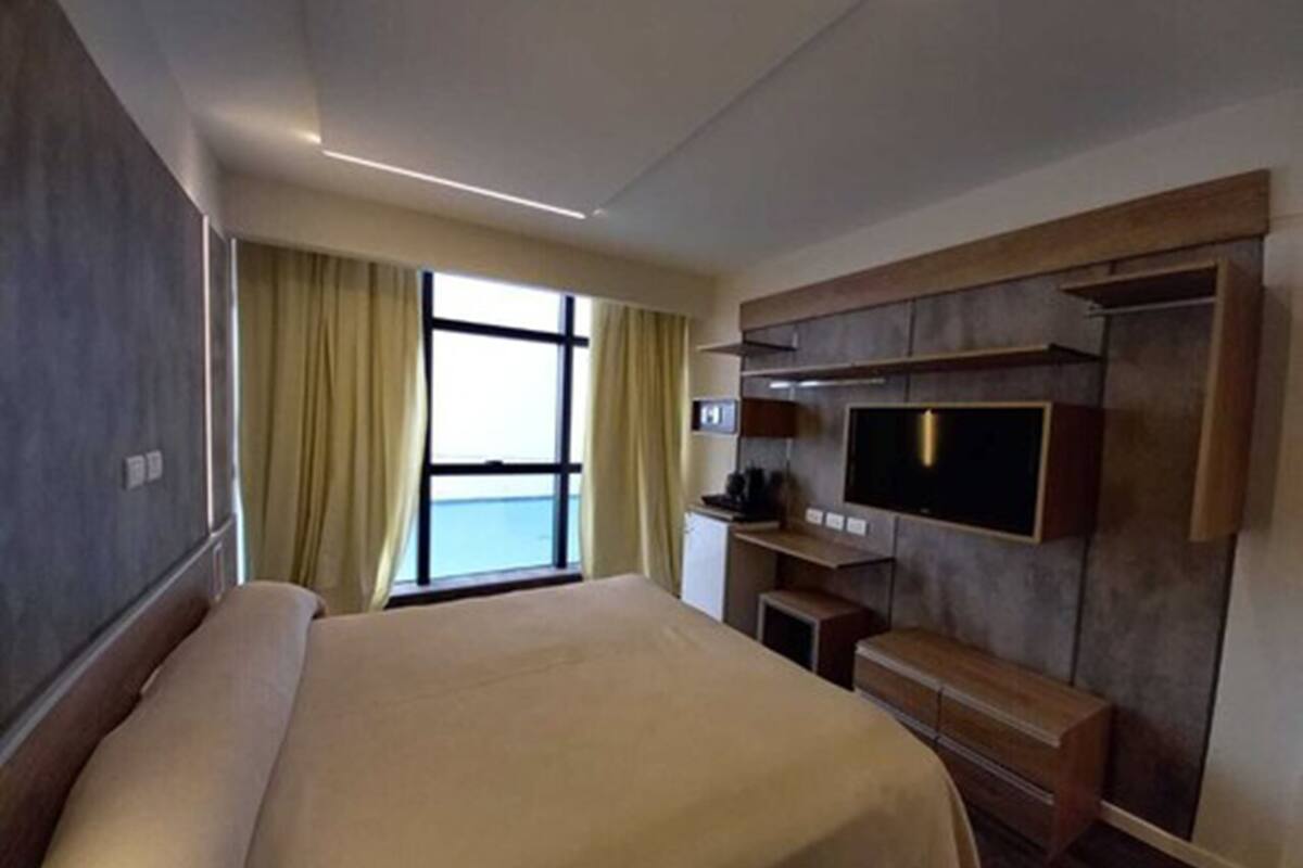 Una habitación de hotel moderna con una cama grande, un televisor en la pared y vistas al mar a través de la ventana.