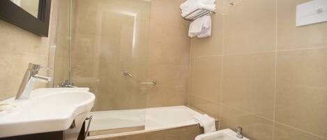 Un baño moderno con cabina de ducha de vidrio, bañera, bidé y tocador con dos lavamanos.