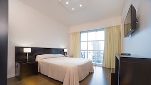 Una habitación de hotel moderna con una cama grande, mesitas de noche con lámparas, un televisor de pantalla plana en la pared y un balcón con cortinas.