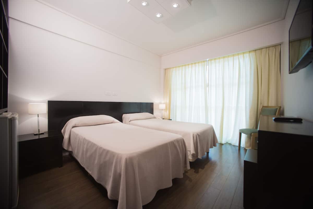 Una habitación de hotel con dos camas, un escritorio, una silla y un televisor.