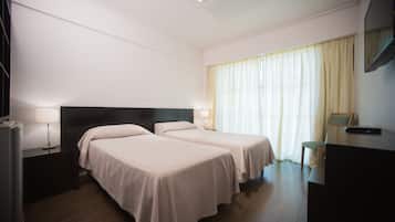 A hotel room with two beds, a desk, a chair, and a TV.
