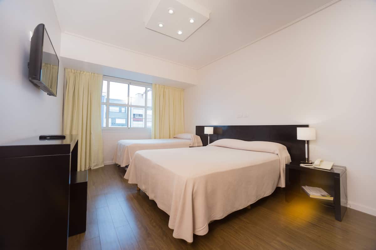 Habitación de hotel con dos camas, un escritorio, un televisor y una ventana con cortinas.
