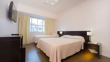 A hotel room with two beds, a desk, a TV, and a window with curtains.