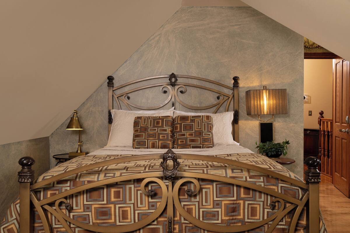A bedroom with a bed, a nightstand, a lamp, and a door.