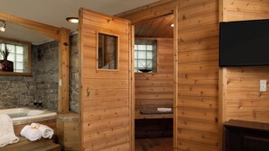 A wooden cabin interior with a stone wall, a wooden bathtub, a fireplace, and a television mounted on the wall. - The Historic Webster House (Bay City)