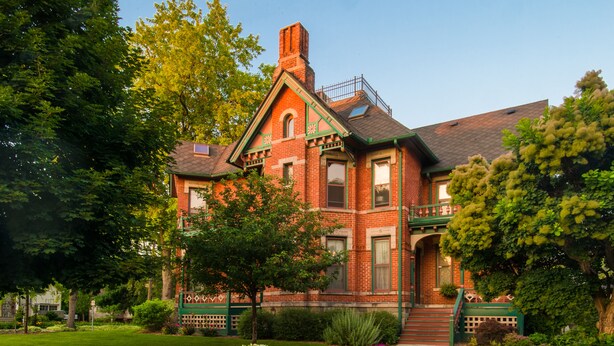 A large, red brick Victorian-style house with a prominent front porch, a second story, and a small balcony. - The Historic Webster House (Bay City)