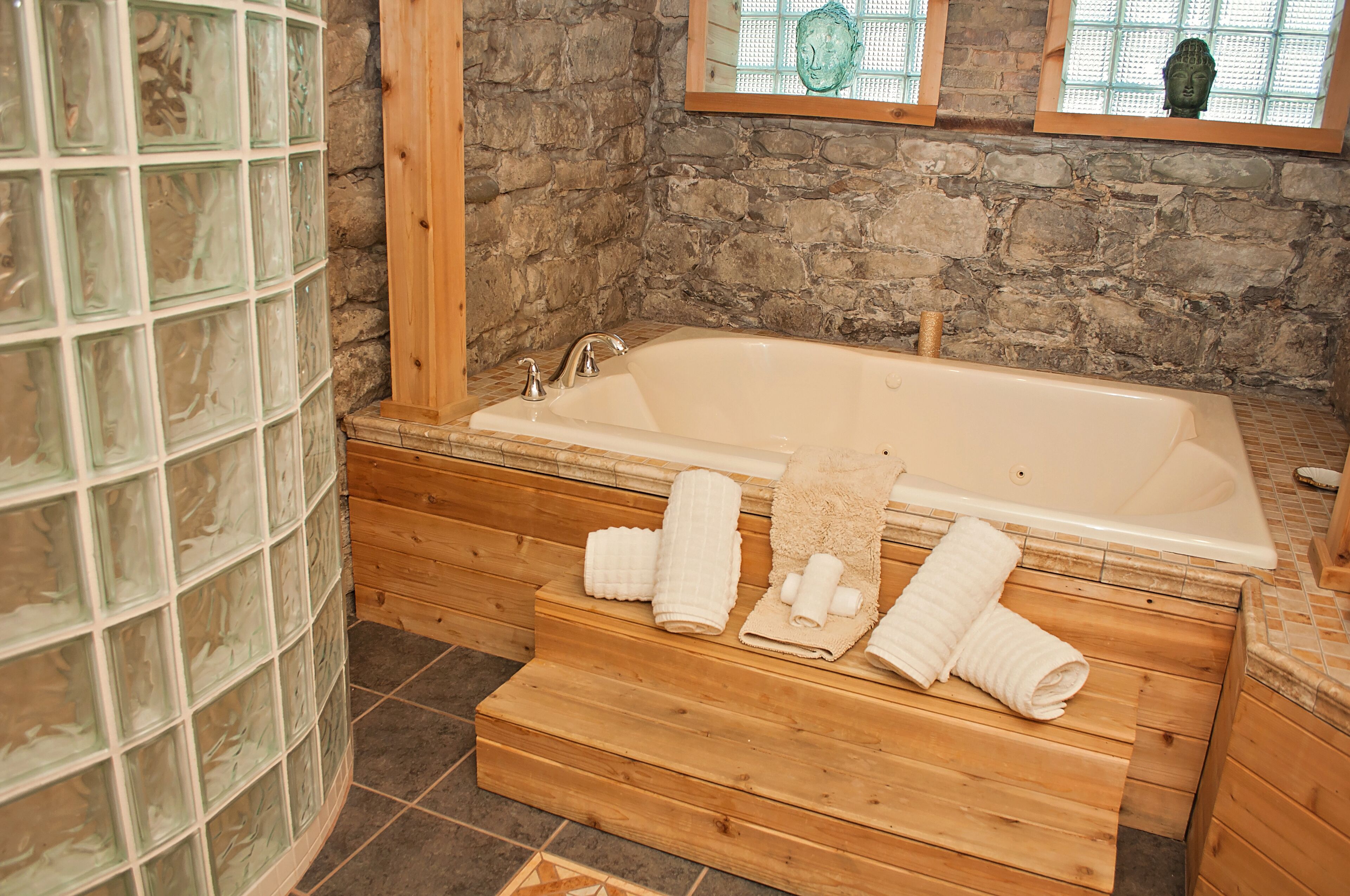 A stone-walled bathroom with a wooden bench, a bathtub, and a glass shower enclosure.