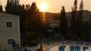 A swimming pool with lounge chairs and a building in the background. - San George (Corfu)