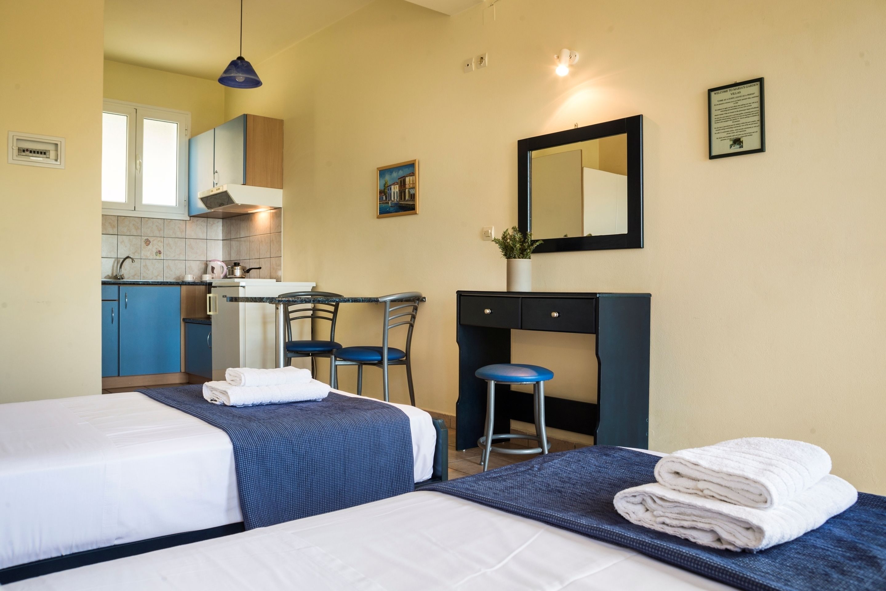 A hotel room with two beds, a desk, a chair, a sink, and a mirror.