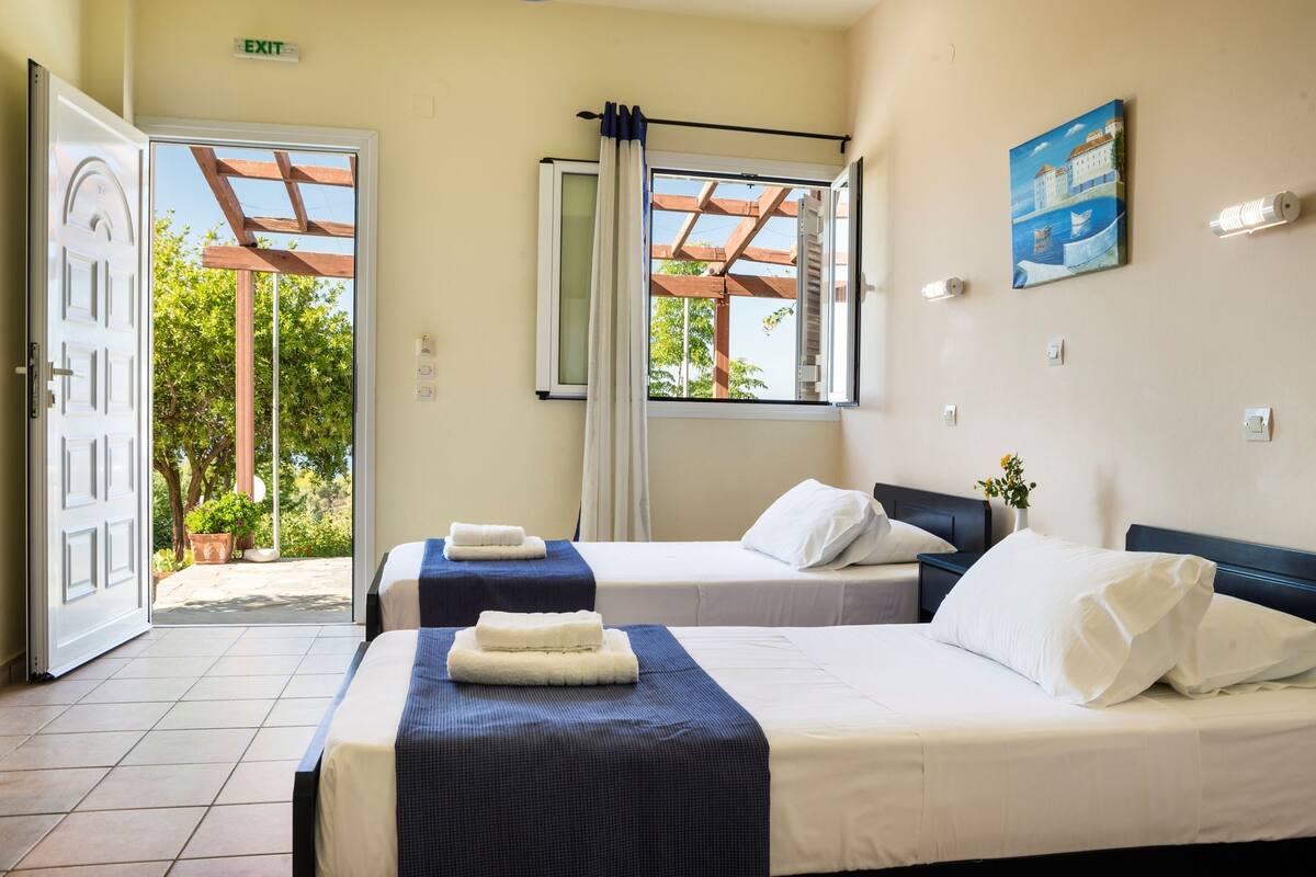 Habitación de hotel con dos camas, una ventana que da a zonas verdes y una señal de salida.