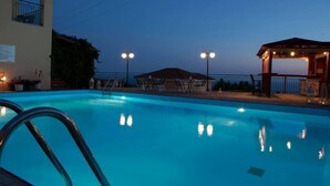 A swimming pool with a view of a mountain at dusk, surrounded by outdoor seating and a gazebo.