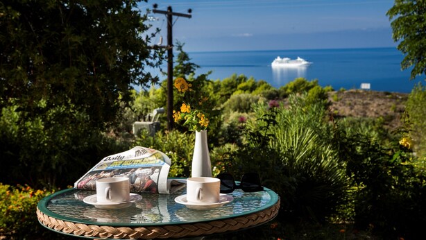 A round table with a newspaper, two cups, and sunglasses.