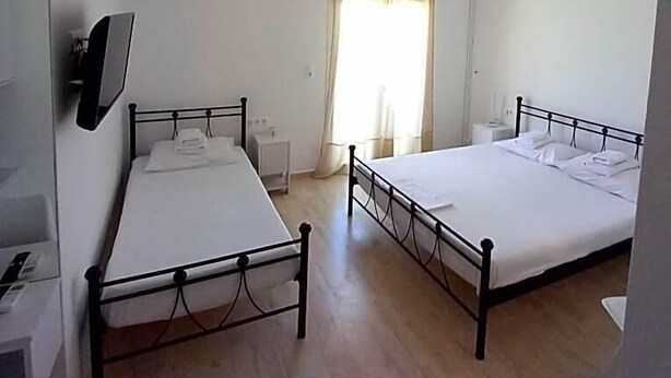 Una habitación con dos camas, televisión montada en la pared, ventana con cortinas y un aire acondicionado blanco.