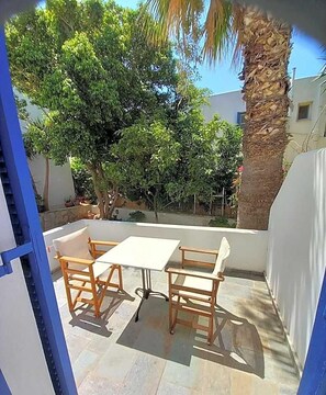 An outdoor patio with a table and chairs, surrounded by trees and a palm tree. - Hotel Naias (Serifos)