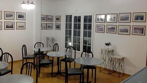 Un comedor con varias mesas y sillas, un ventanal grande y cuadros en las paredes.