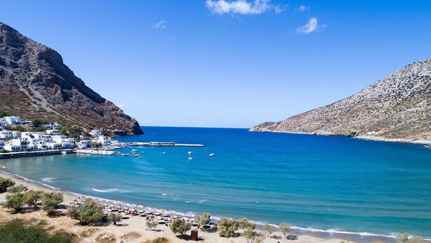 A coastal town with white buildings, a marina, and a beach with umbrellas. - Boufounis Studios (Sifnos)