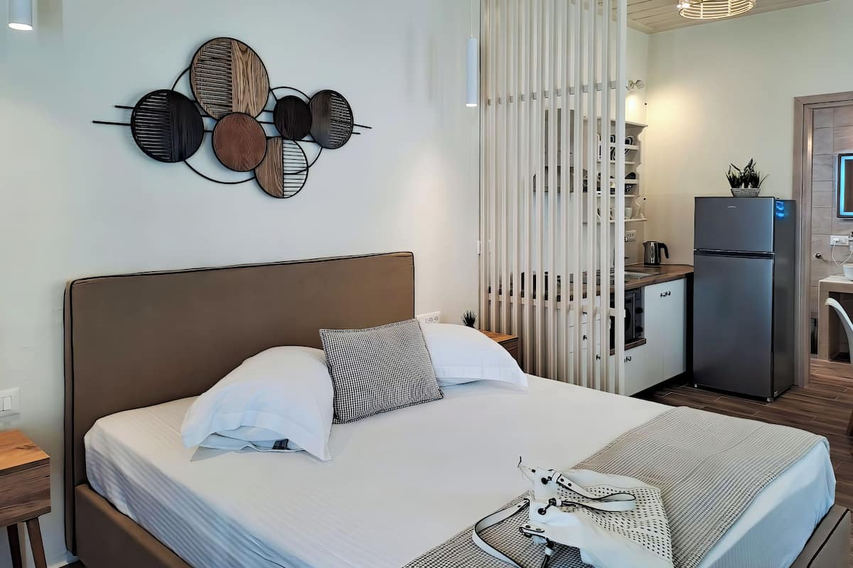 A modern hotel room with a large bed, a wall-mounted decorative piece, a kitchen area, and a refrigerator.