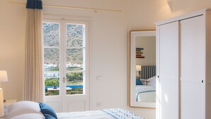 A bedroom with a bed, a window with a view of a hillside, and a wardrobe. - Boufounis Studios (Sifnos)