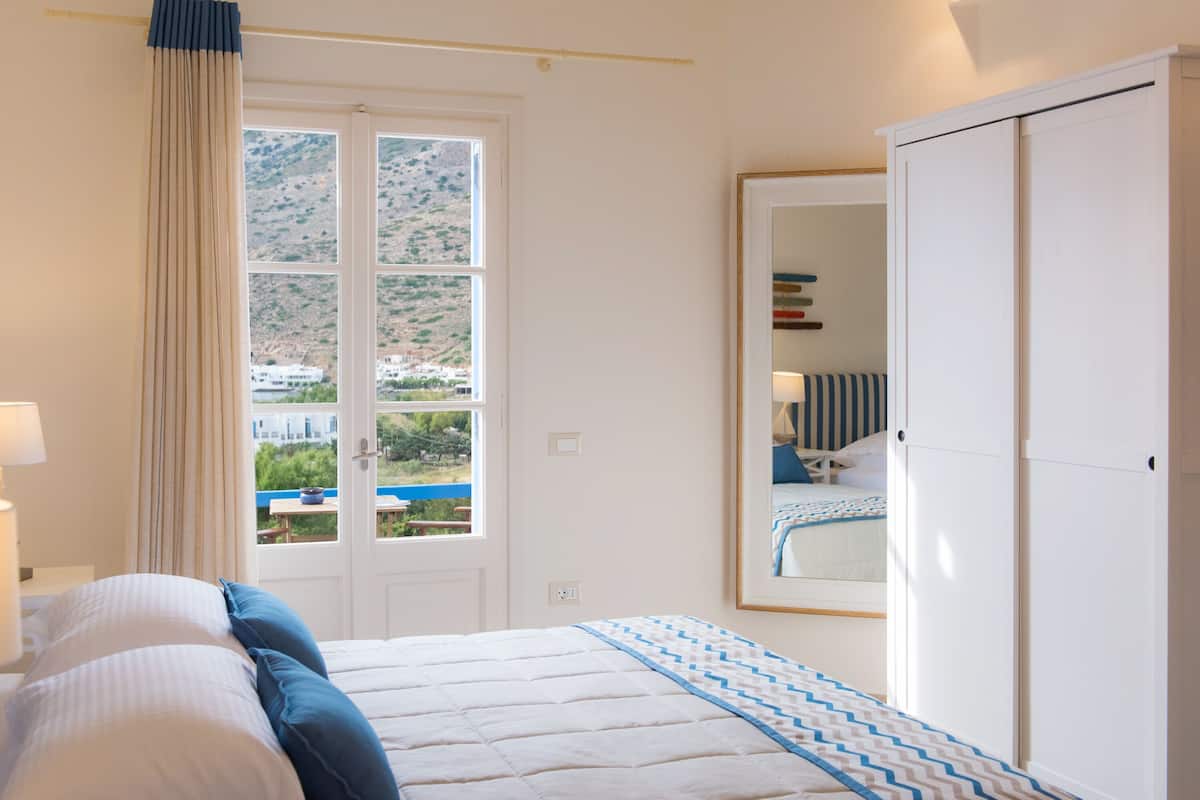 A bedroom with a bed, a window with a view of a hillside, and a wardrobe.