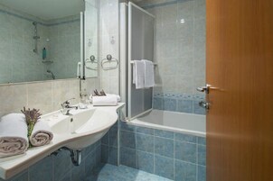 Un baño con lavamanos, espejo, toallero, ducha y bañera.