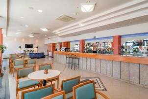 Um saguão de hotel com área de bar, disposição de assentos e uma tela de televisão.