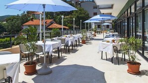 An outdoor terrace with tables and chairs, umbrellas, and potted plants. - Amfora (Labin)