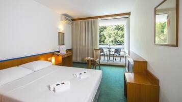 Una camera d'albergo con un letto grande, una scrivania, una sedia e una finestra con vista sul verde.
