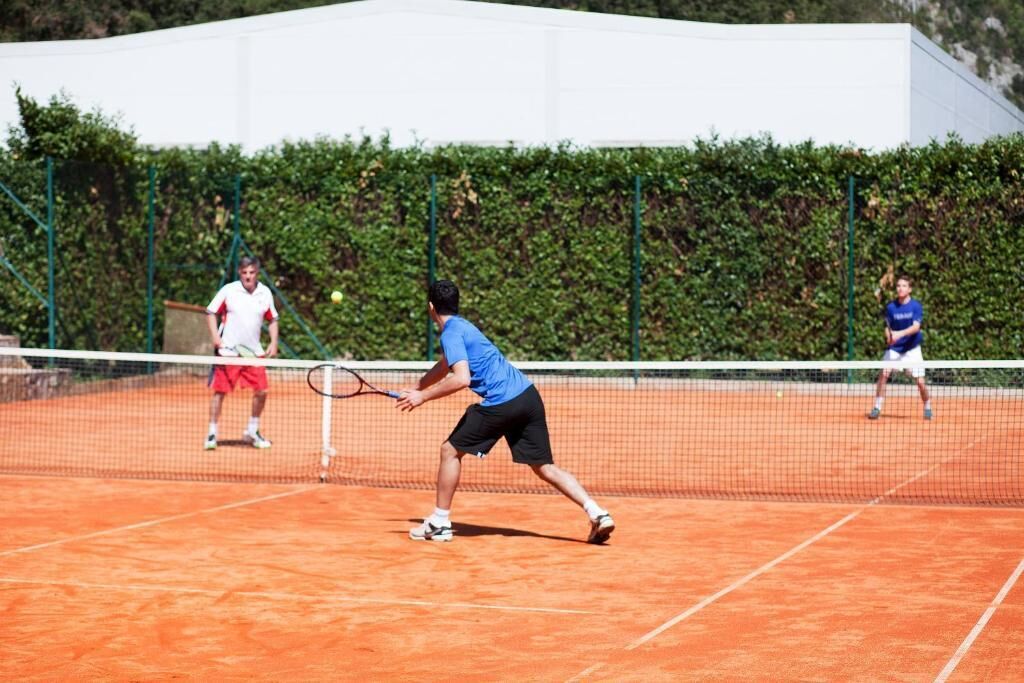 Ein Tennisplatz mit Netz in der Mitte, umgeben von einer grünen Hecke.