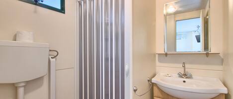 A bathroom with a toilet, a shower curtain, a sink with a mirror above it, and a window above the shower.