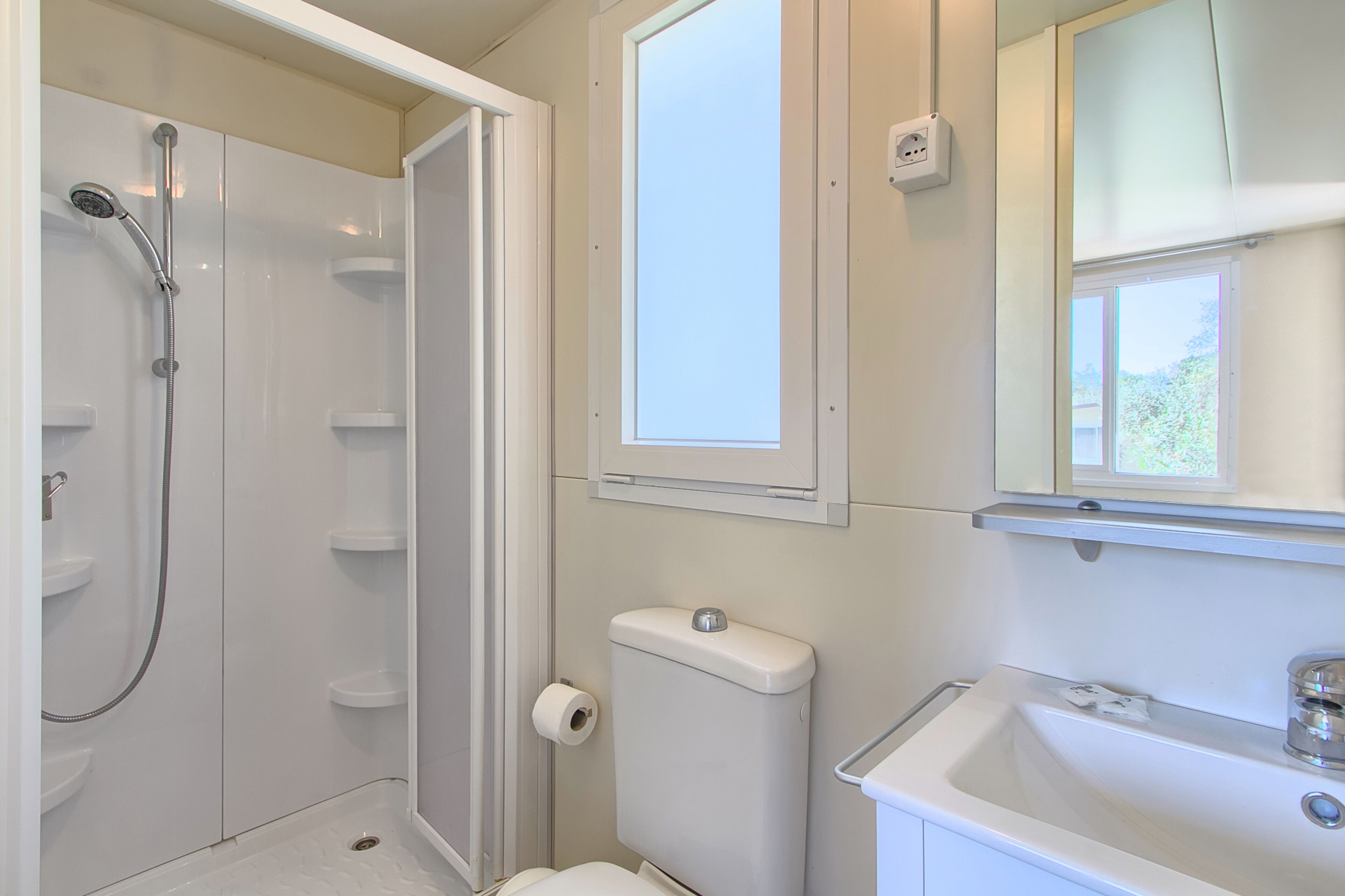 A bathroom with a shower, toilet, sink, and a window above the mirror.