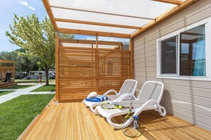 A covered outdoor area with two white lounge chairs, a tennis racket, and a hat on one of the chairs. - Camping Oliva Mobile Homes (Labin)