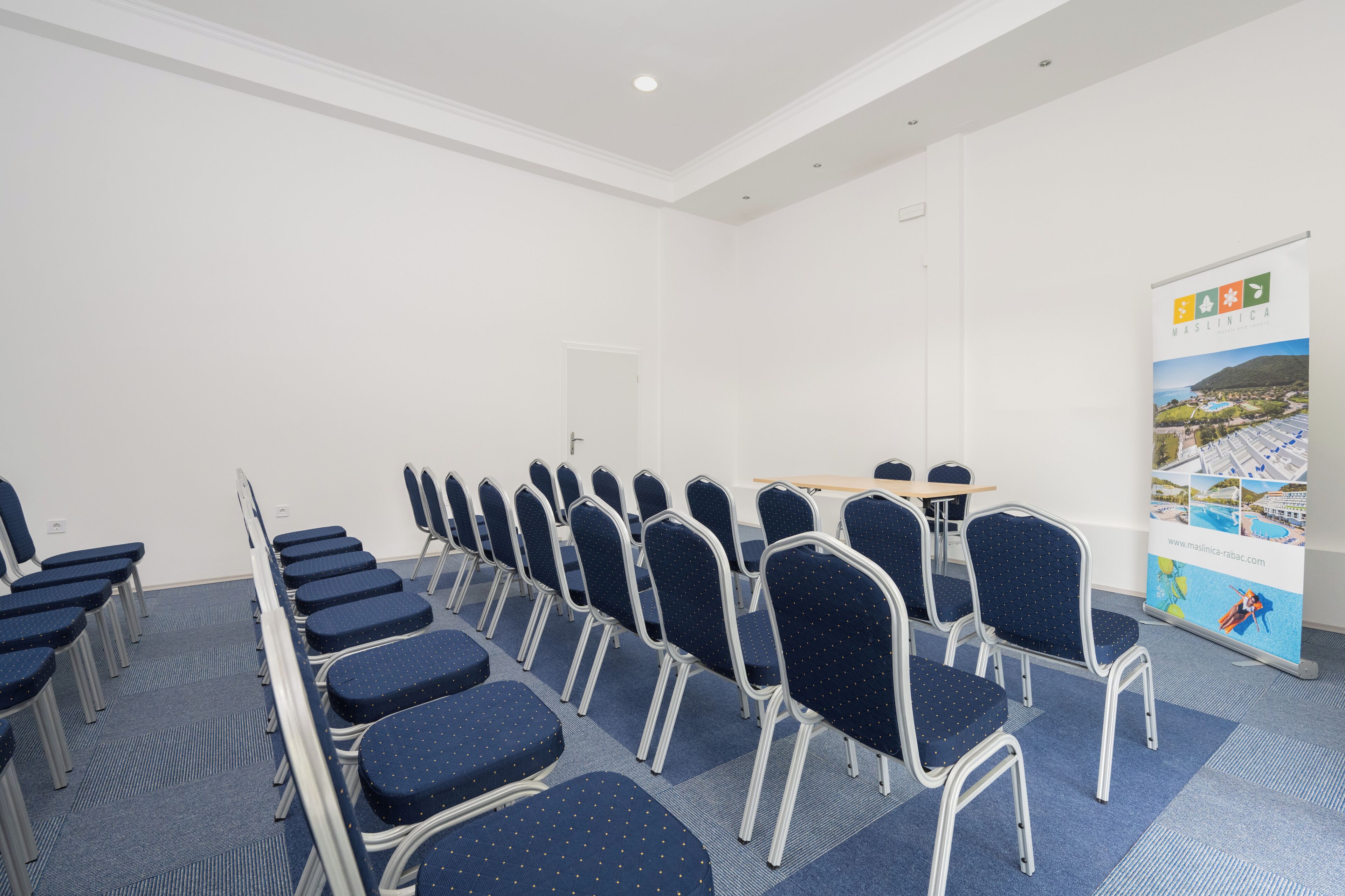 A conference room with rows of chairs, a table, and a banner.