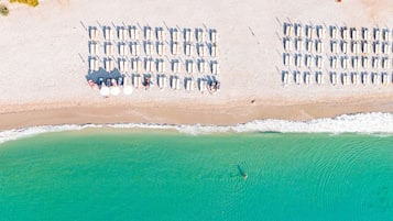 Una vista aerea di un resort sulla spiaggia, con file di sdraio, una spiaggia sabbiosa e un mare turchese cristallino.