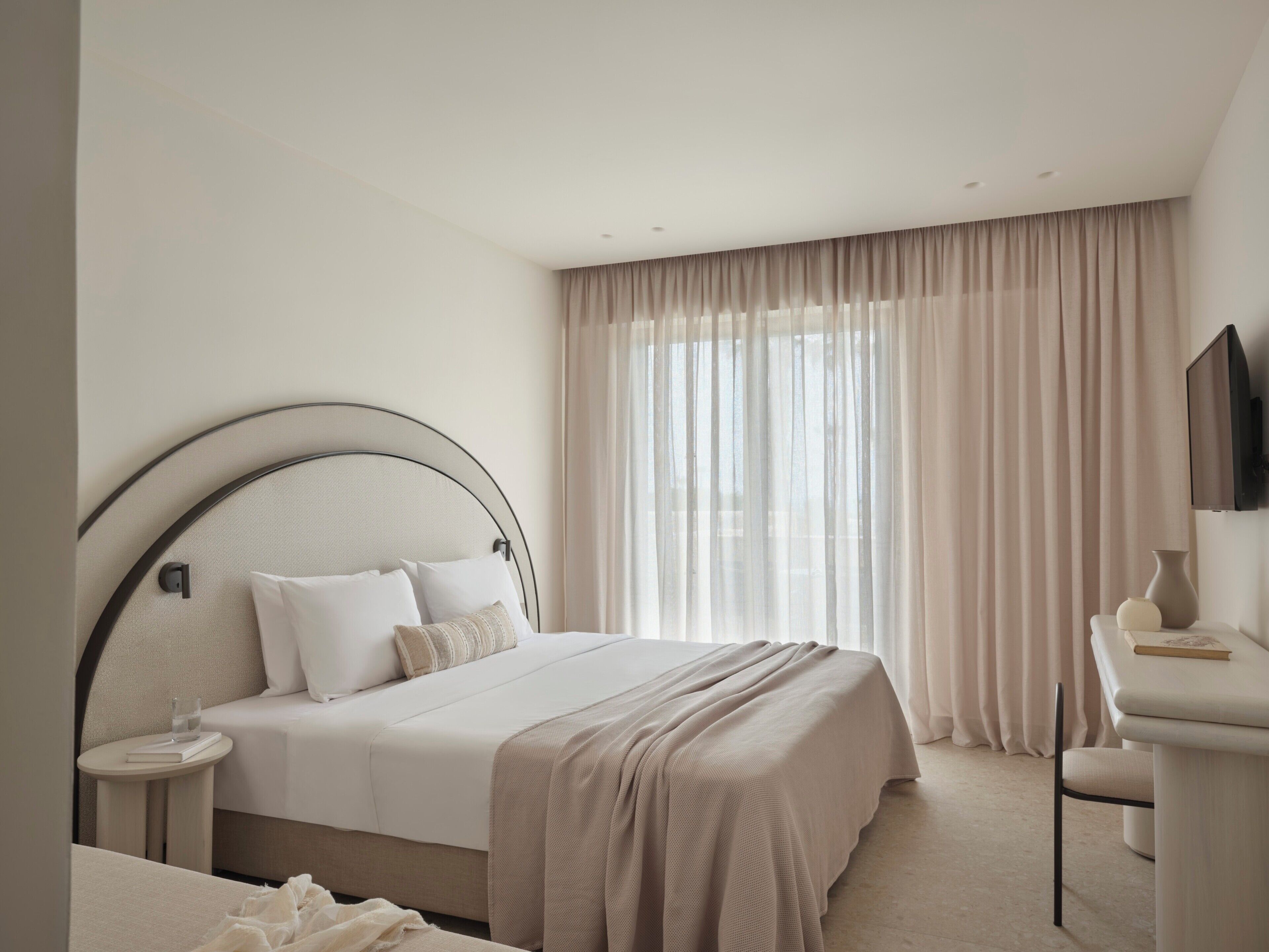 Une chambre d’hôtel avec un lit, une table de chevet sur laquelle se trouve un verre d’eau, une chaise et un téléviseur fixé au mur.