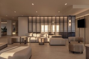 Un intérieur moderne avec un canapé d’angle, des poufs et un téléviseur à écran plat fixé au mur.