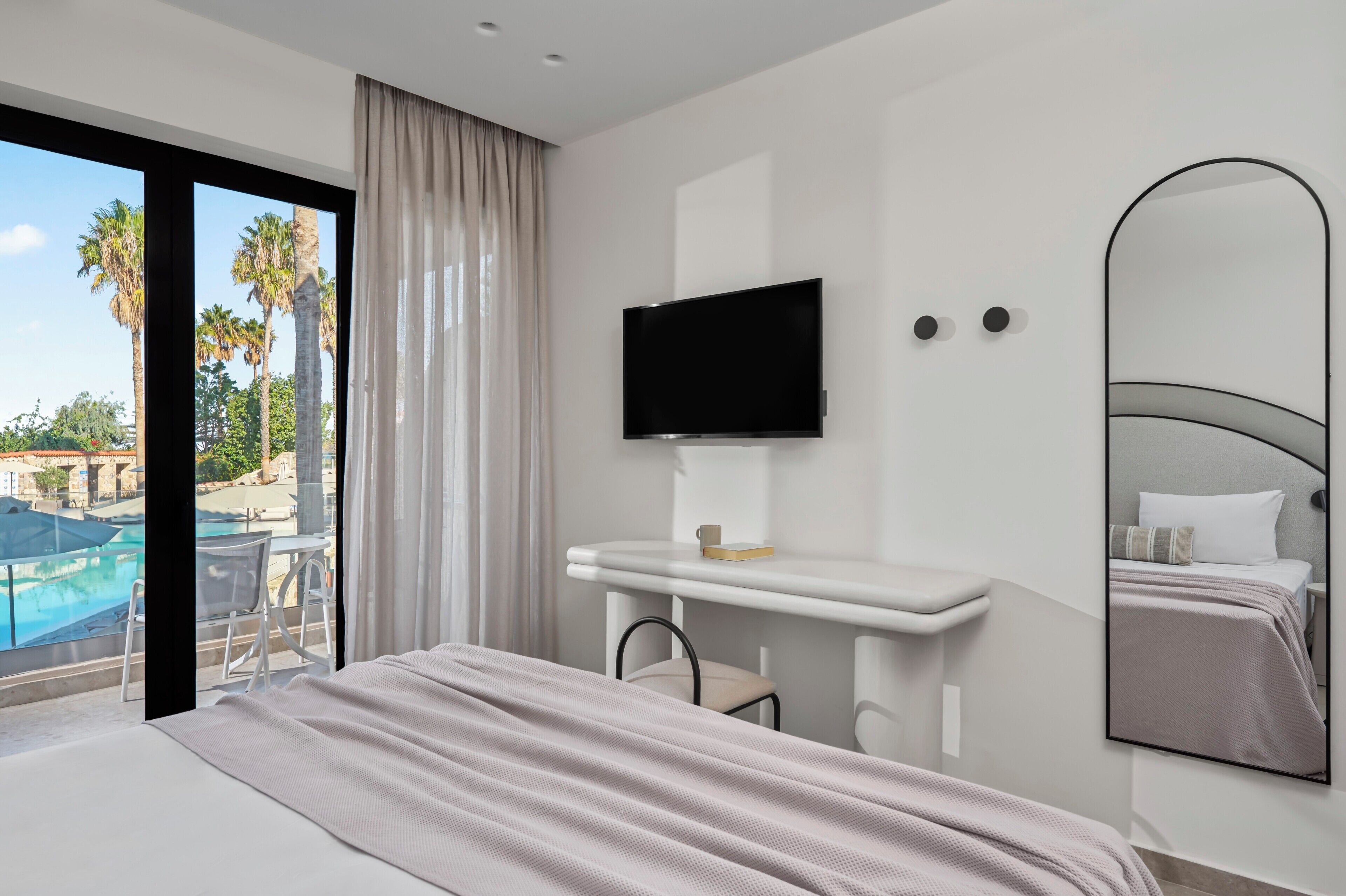 Ein modernes Hotelzimmer mit Bett, Fernseher, Schreibtisch und großem Fenster mit Blick auf einen Pool.