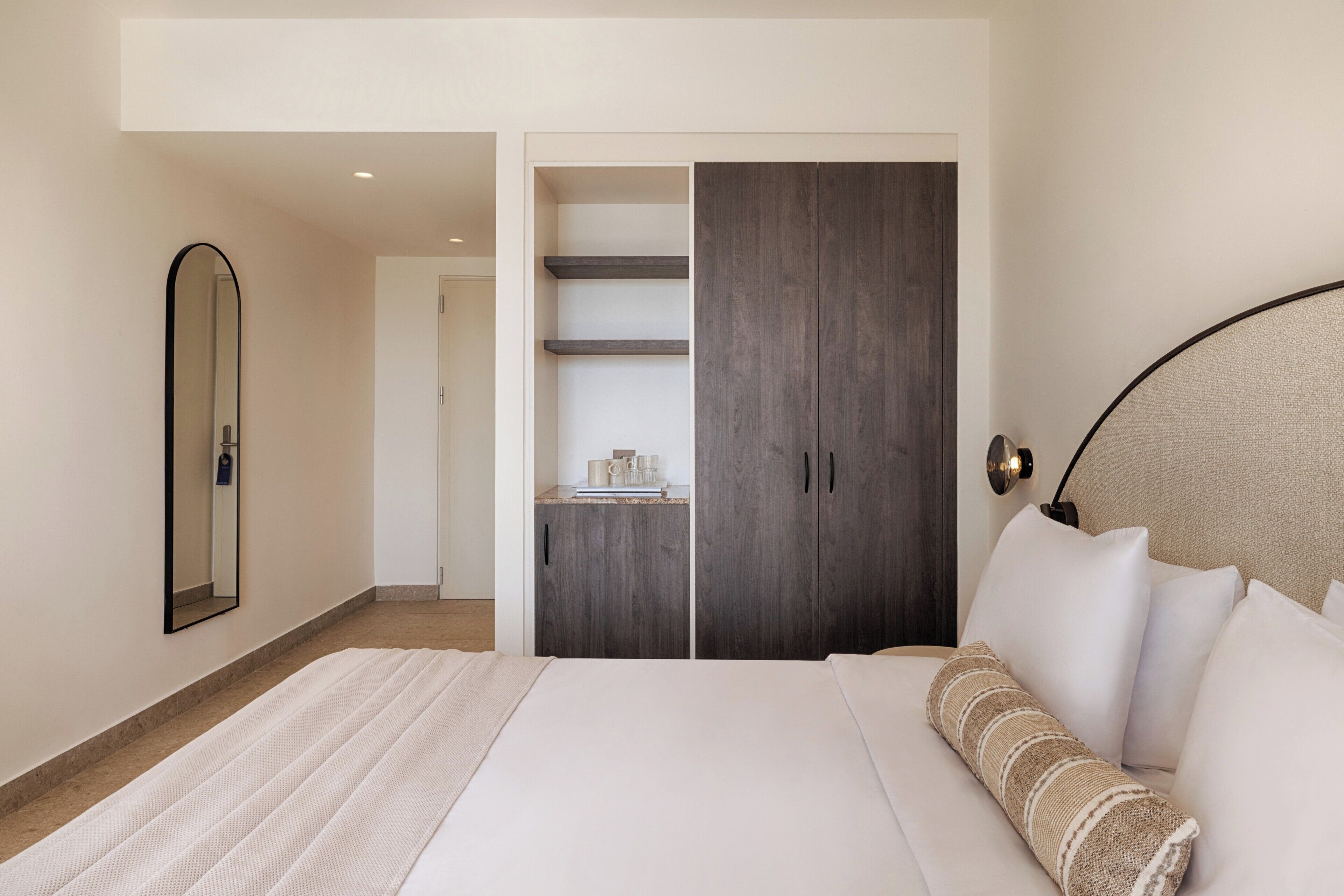 Un dormitorio con cama, armario, espejo y mesita de noche.