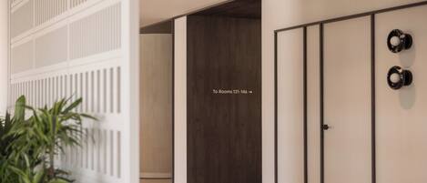 Een gang met een richtingwijzer naar kamers 121-146, een plant en een deur met een zwarte handgreep.