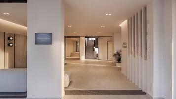 A modern hotel lobby with a neutral color palette, a reception desk, a staircase, and a sign indicating the hotel is operated by Wavemaker Hospitality.