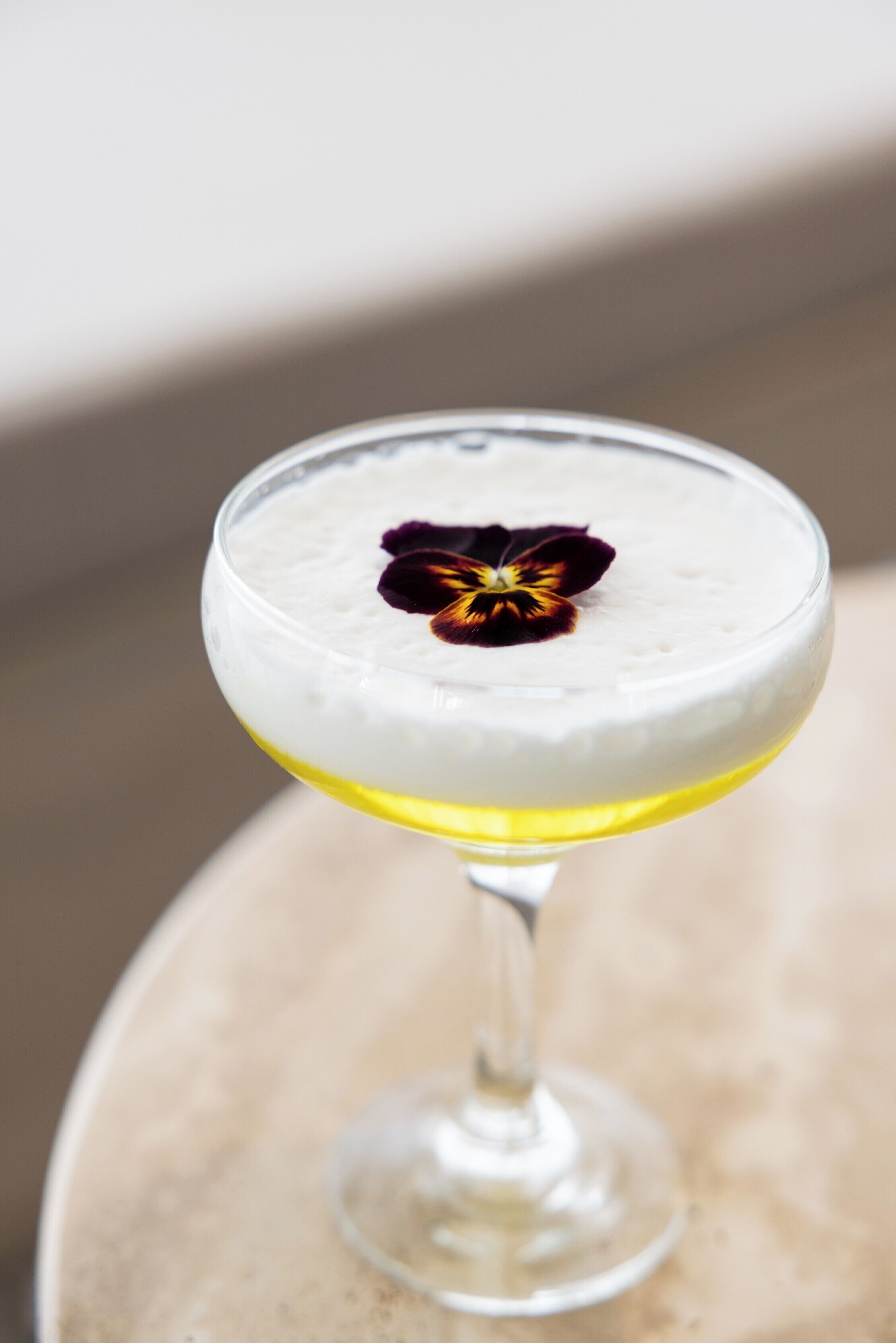 Un cocktail servi dans un verre à pied, décoré d’une fleur.