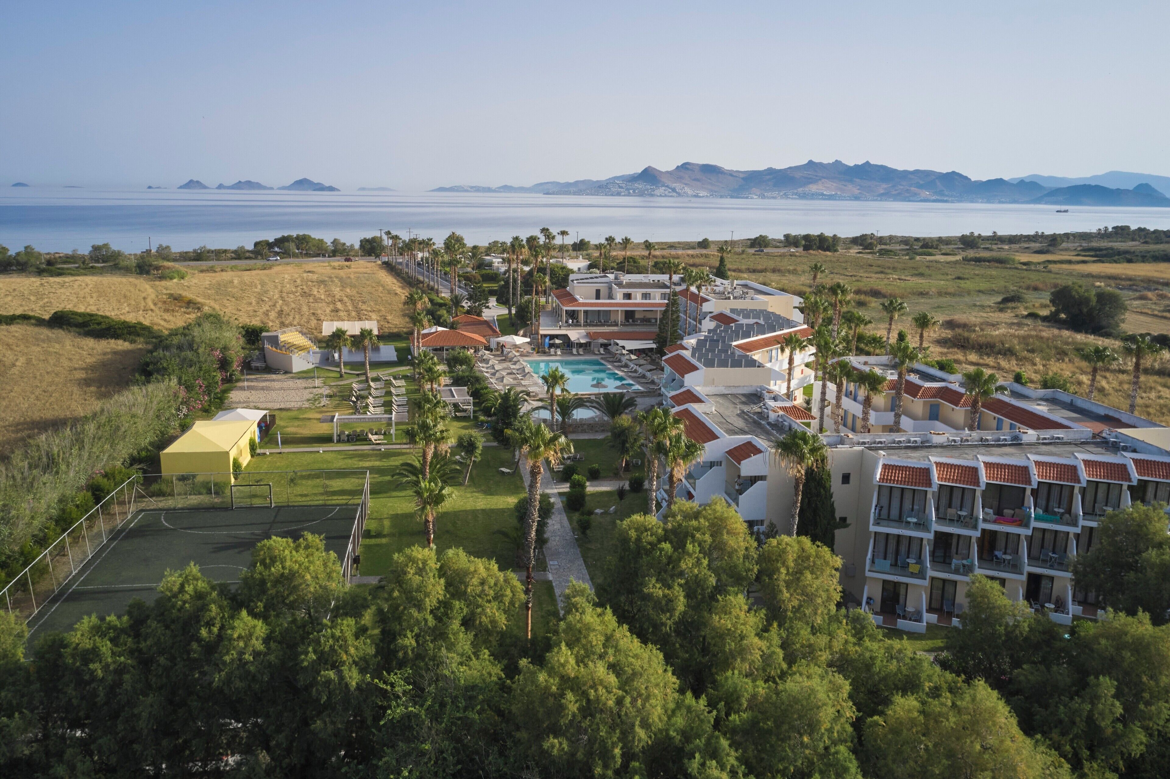 Un resort con piscina, cancha de tenis y varias edificaciones con balcones.