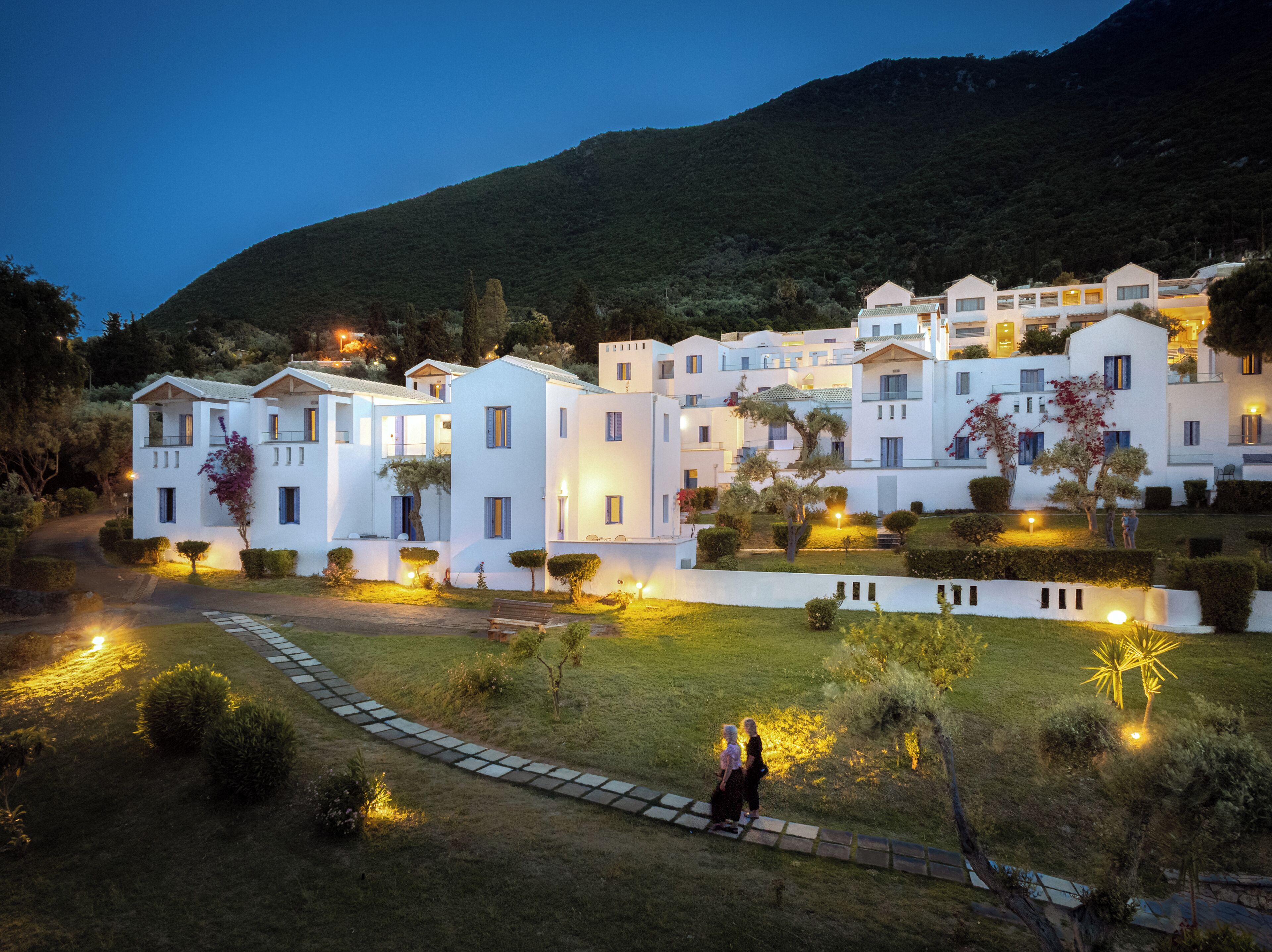 Un complex residencial amb diverses edificacions blanques, un camí pavimentat i vegetació ben cuidada.