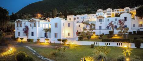 A residential building complex with multiple white structures, a paved pathway, and well-maintained greenery.
