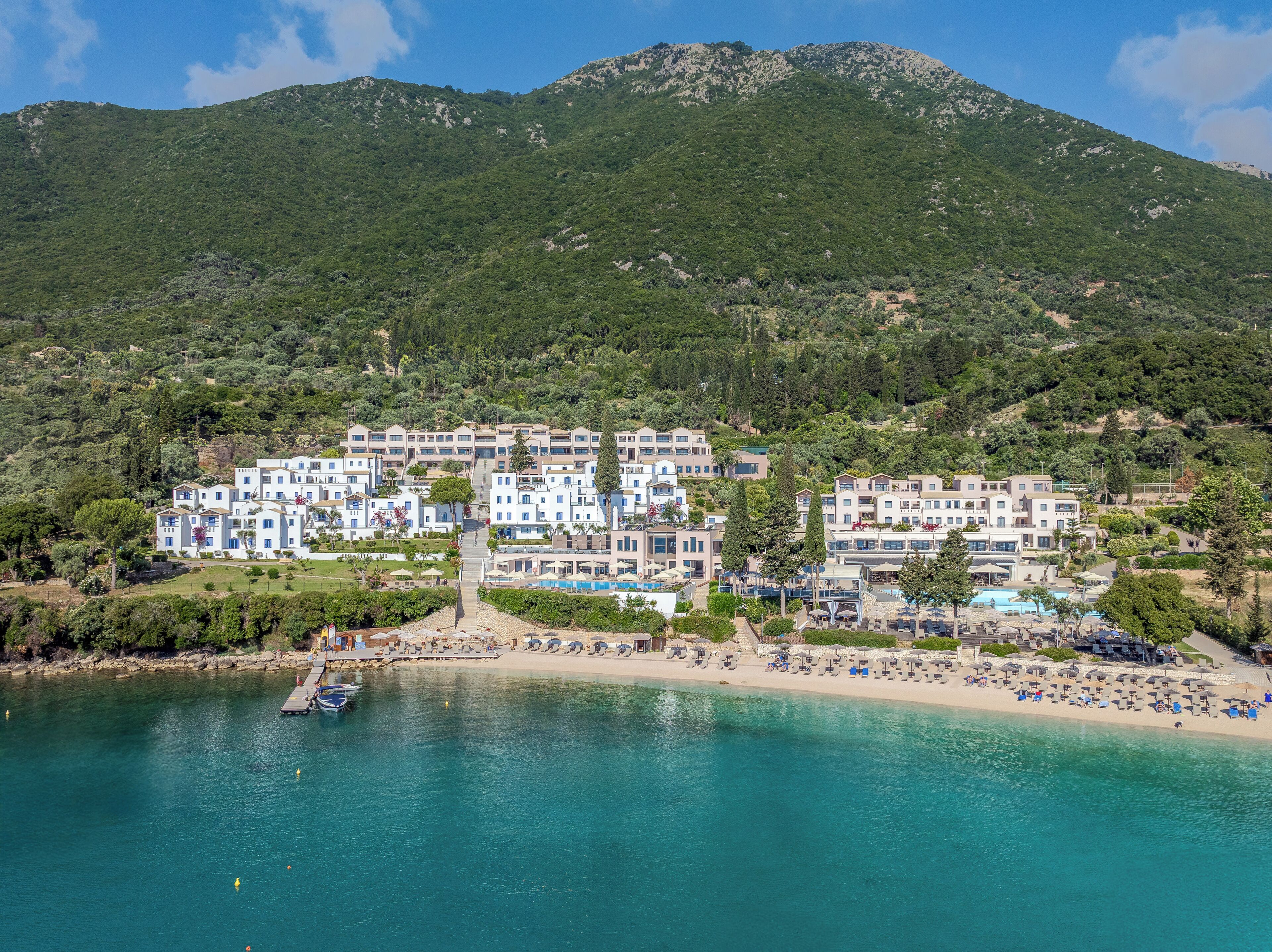A coastal hotel with multiple buildings, a beach, and a mountain in the background.